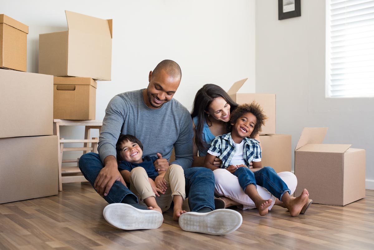 A family of four sitting on the floor among moving boxes.