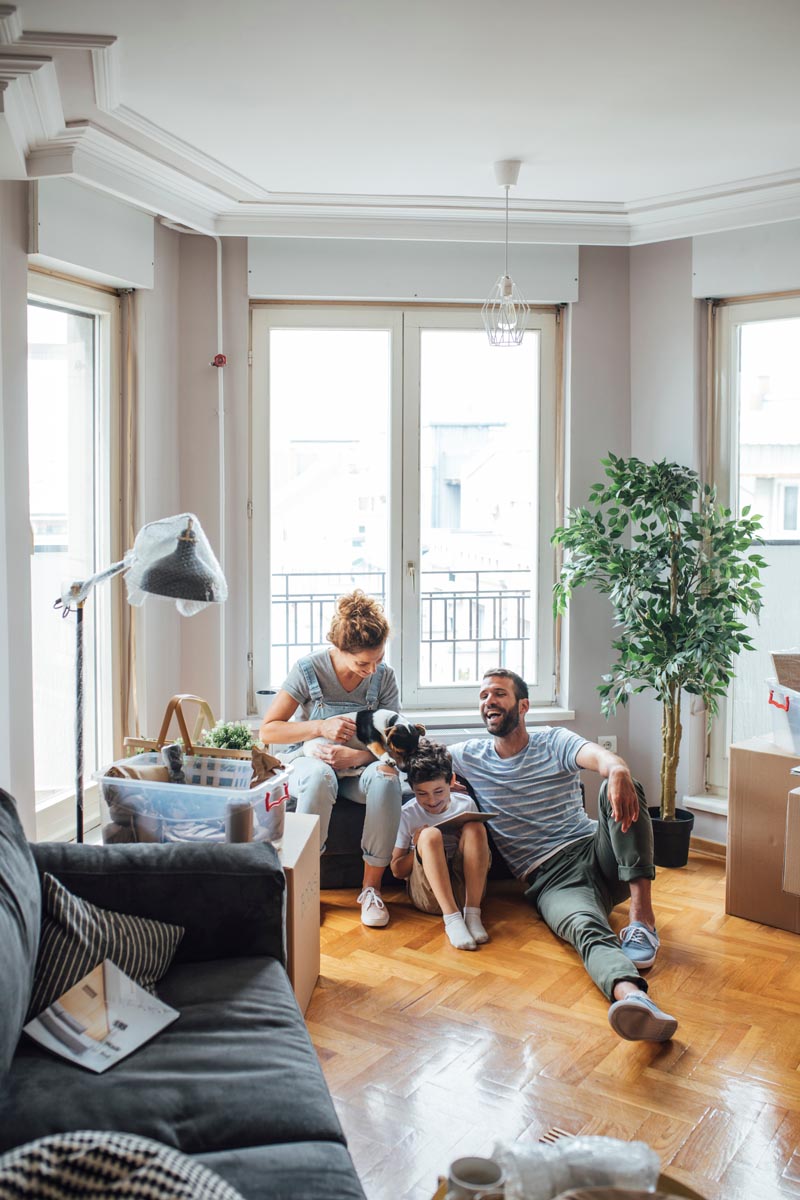 A family sitting on the floor of a sunlit room with a small dog.