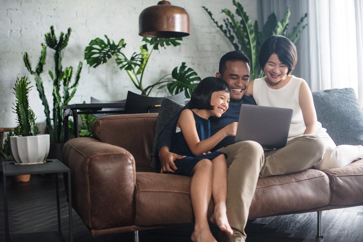 A family of three looking at a laptop together on a brown sofa.