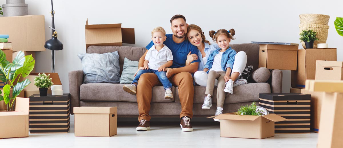 A family of four sitting on a sofa surrounded by moving boxes.