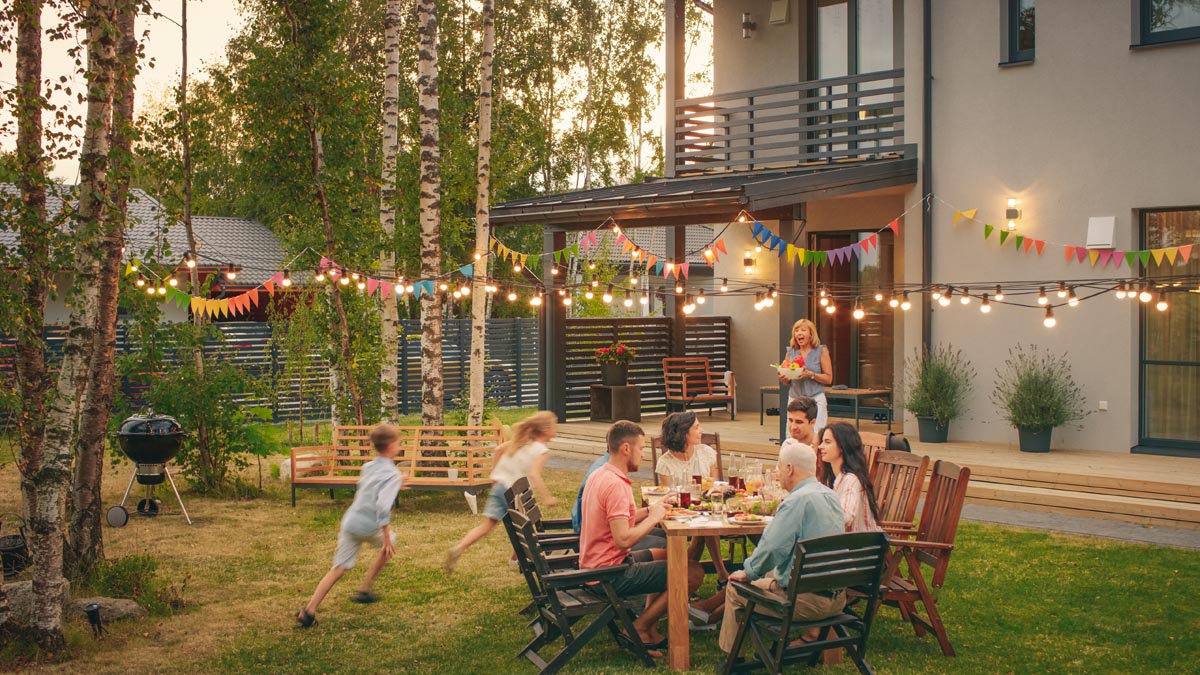People gathered around an outdoor table under string lights, with children running nearby.