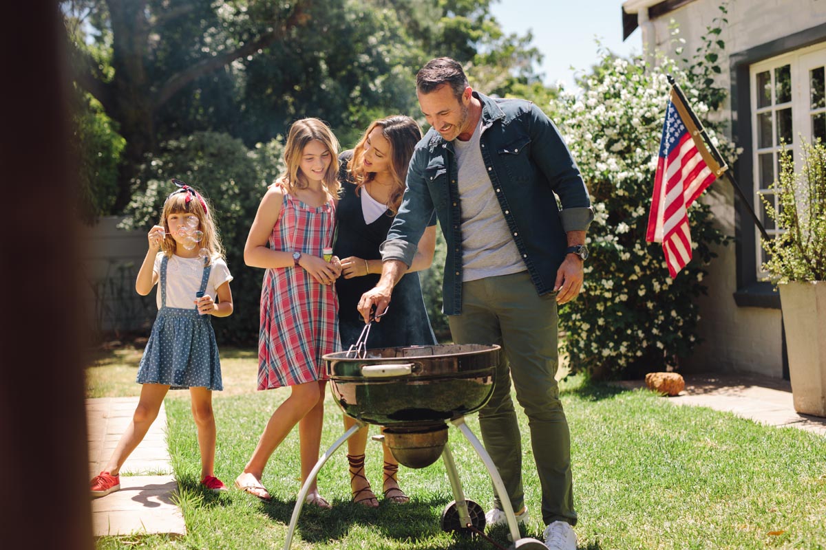 A family standing around a grill in a backyard.