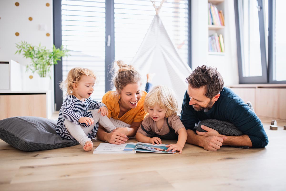 Parents and two small children lying on the floor, looking at a picture book.
