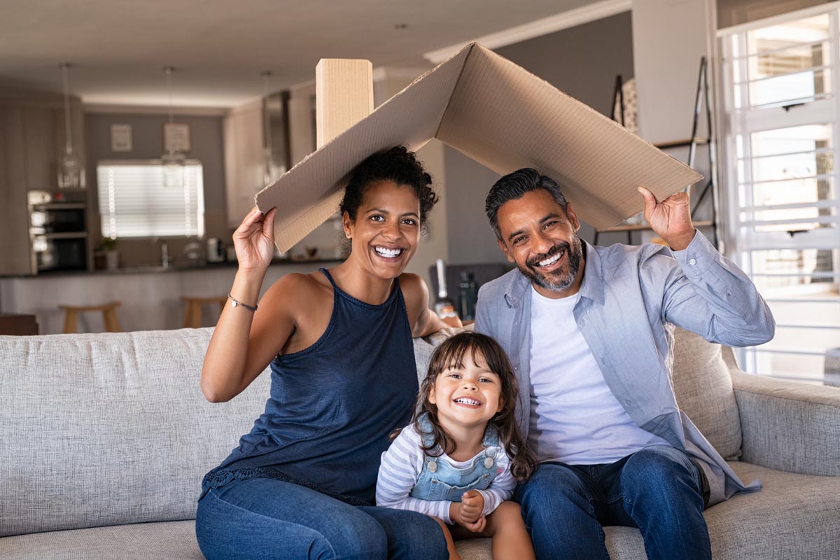 A family on a sofa holding a cardboard roof over their heads.