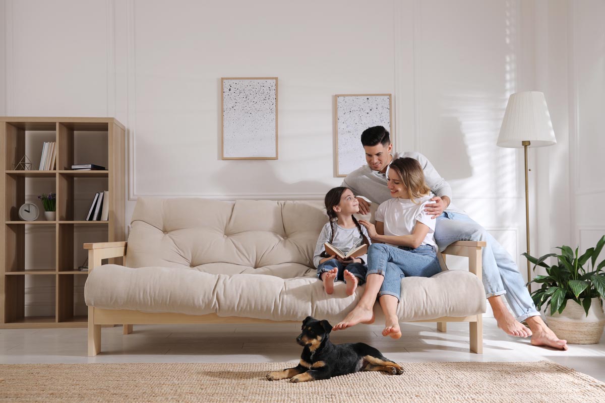 A family on a sofa with a dog lying on the rug in front of them.