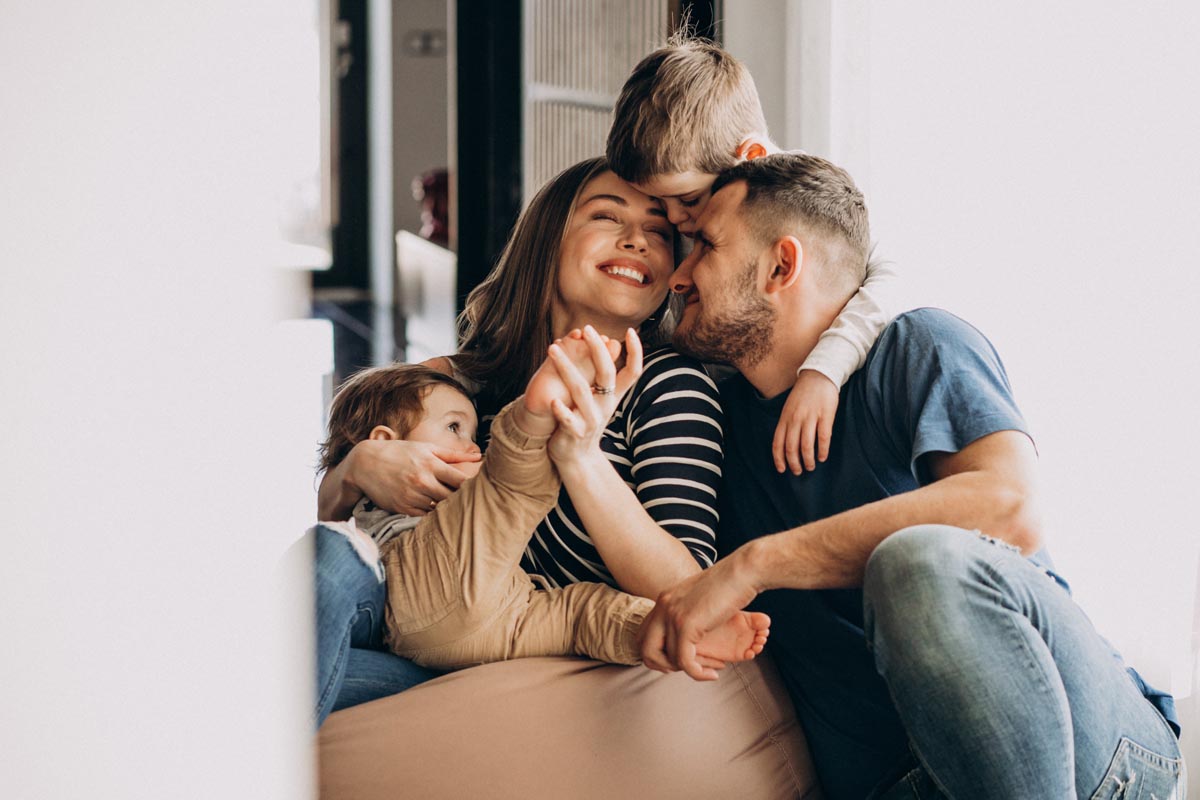 A family of four sitting close together on a beanbag in a bright hallway.