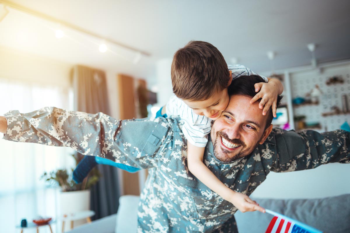 A child sitting on the shoulders of a parent in a camouflage uniform.