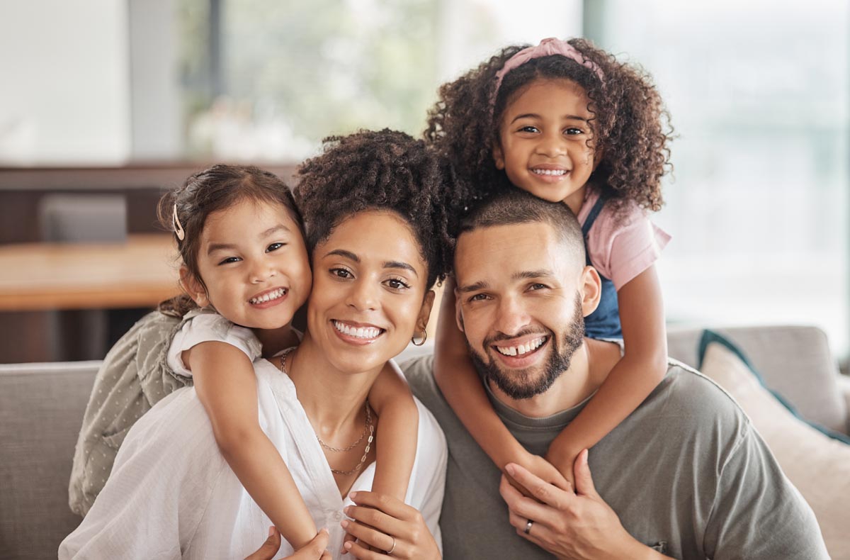 A family of four close together on a sofa, two children on their parents’ shoulders.