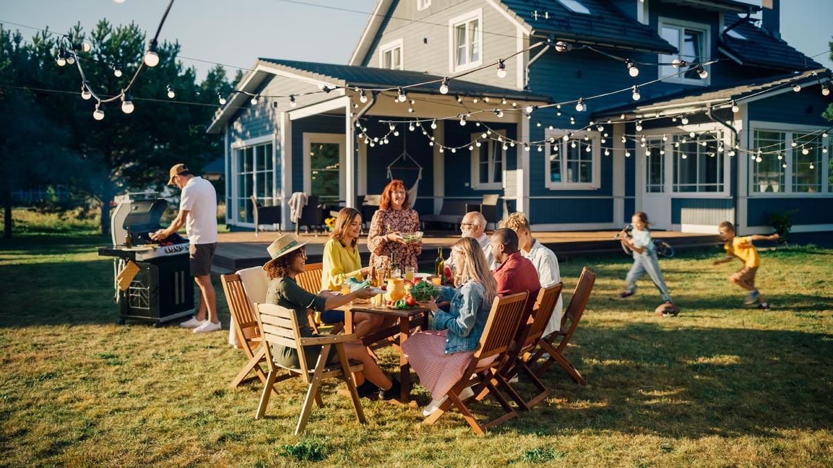 A family gathered around an outdoor table in front of a blue house.