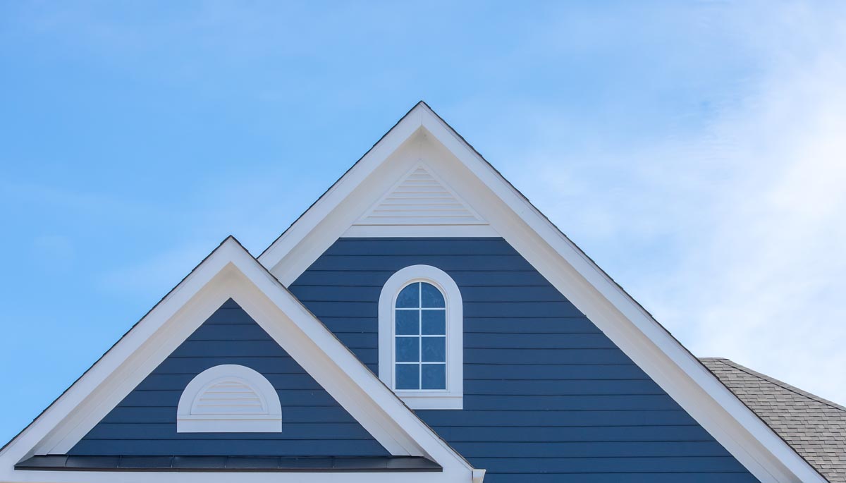 The gable of a blue house with white trim and an arched window.