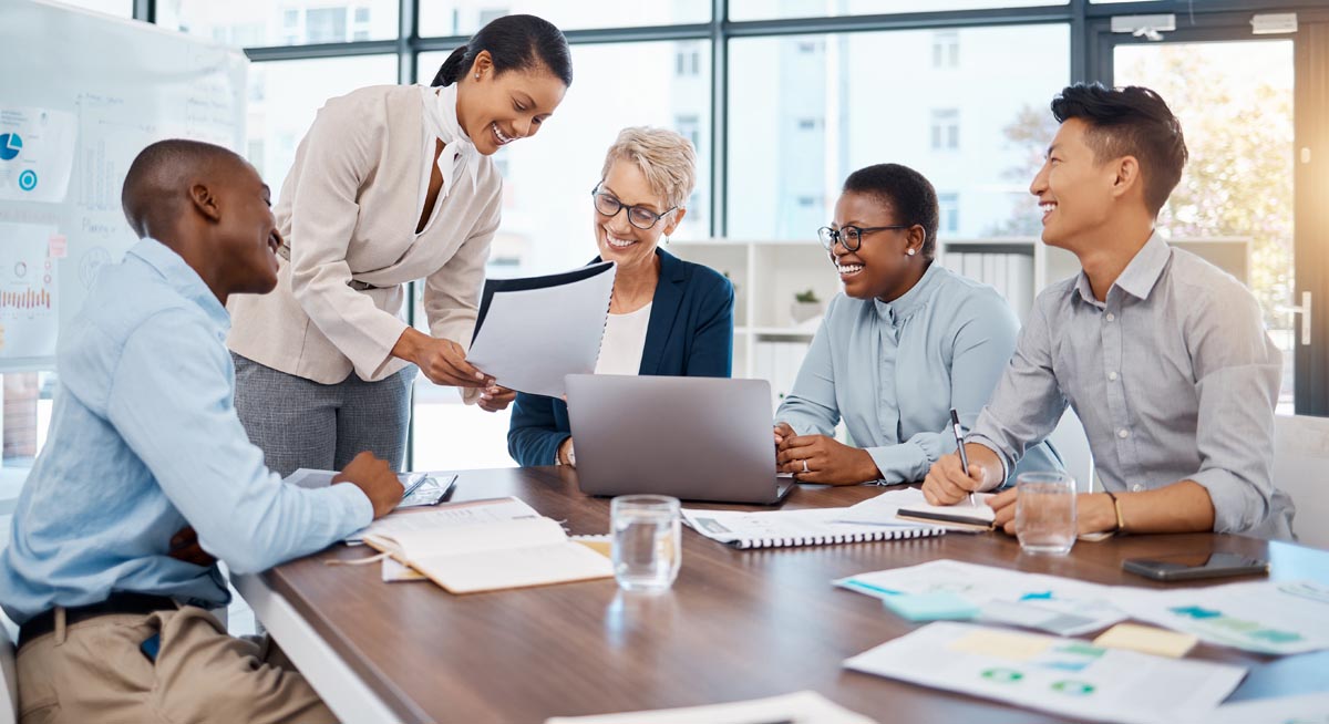 Five coworkers reviewing papers around a conference table.