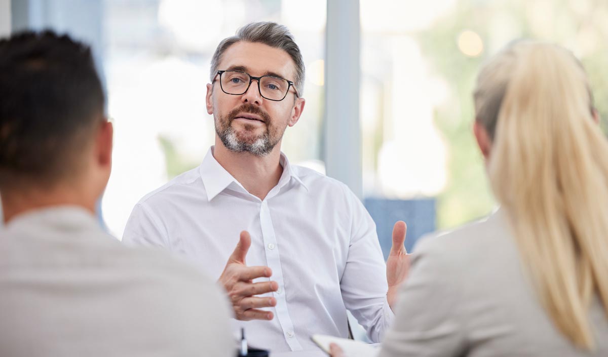 A man in a white shirt explaining something to two people seated across from him.