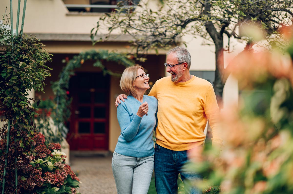 An older couple walking in front of their house.
